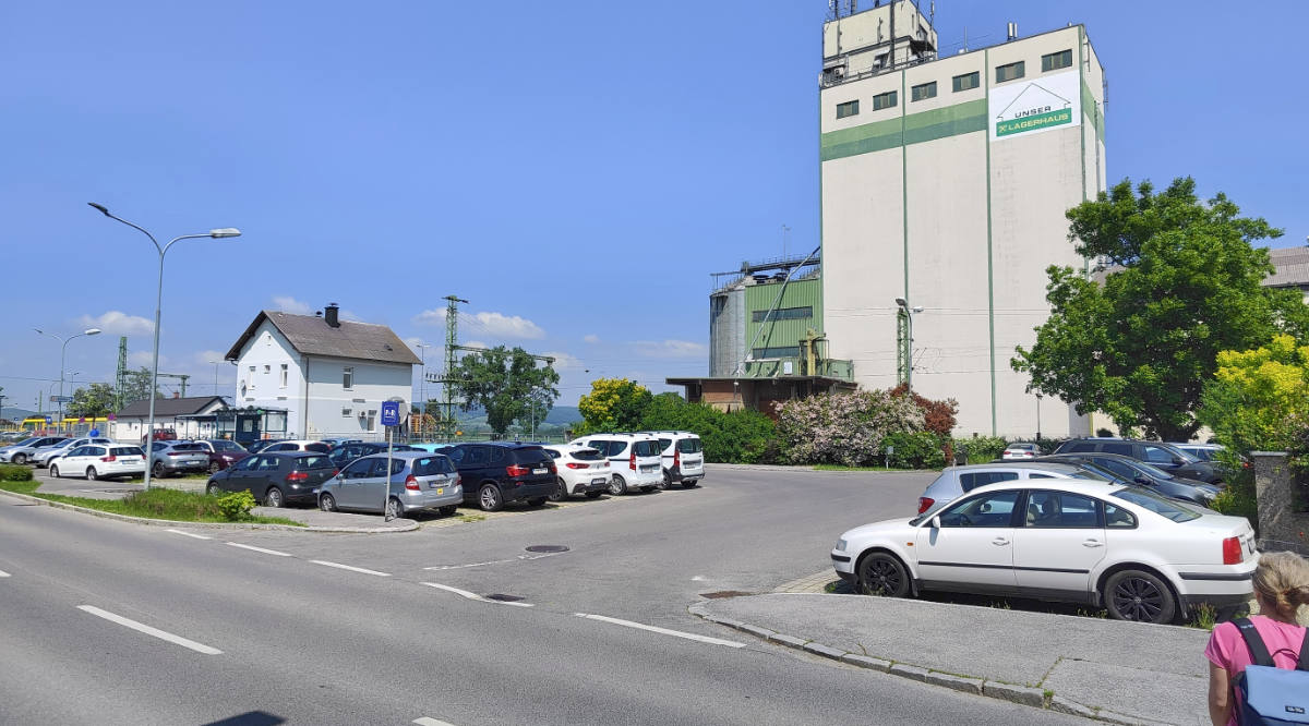 Bahnhof Deutschkreutz mit asphaltierten baumlosen Park & Ride -Parkplatz voll mit Autos belegt